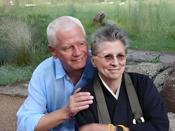 Older couple outdoors, man smiling and woman with glasses.