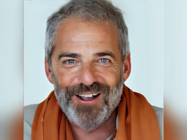 Smiling middle-aged man with gray hair and beard wearing an orange scarf.
