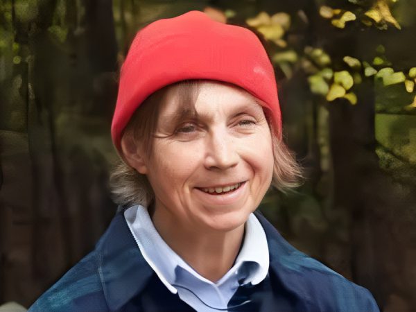 Smiling person wearing a red beanie and blue jacket outdoors.