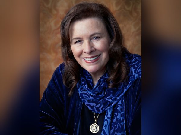 Smiling woman with brown hair wearing a blue scarf and pendant necklace.