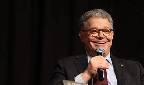 A man with glasses speaking into a microphone on stage.