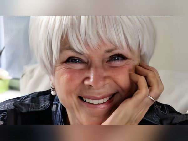 Smiling elderly woman with silver hair resting her face on her hand.