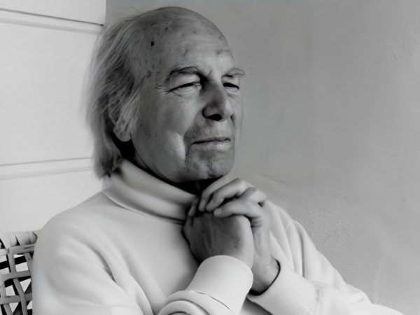 Elderly man with closed eyes and clasped hands in thoughtful pose.