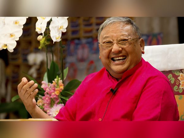 A joyful elderly man in a bright pink shirt laughing warmly.
