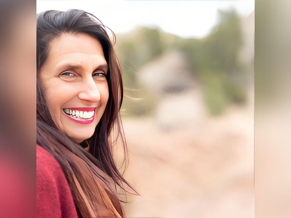 A woman with long dark hair smiles brightly outdoors.