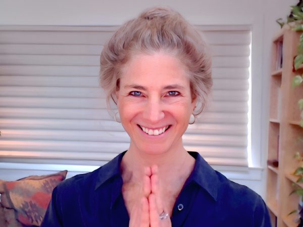 Smiling woman with hands in a prayer position, wearing a dark top.