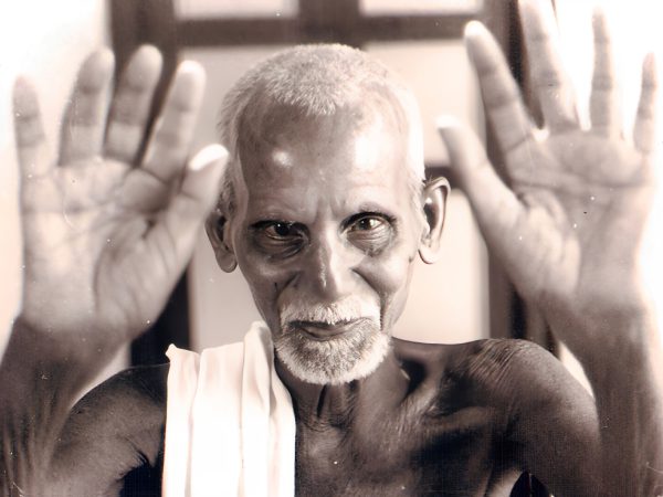 Black-and-white photo of an elderly man with hands raised towards the camera.