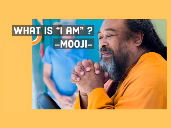 Mooji smiling and clasping hands with a text overlay asking about the meaning of 'I am'.