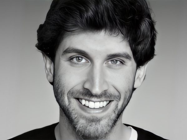 Close-up portrait of a smiling man with dark hair and beard.