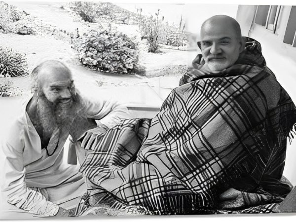 Two elderly men in traditional attire sitting outdoors, one with a beard and the other bald.