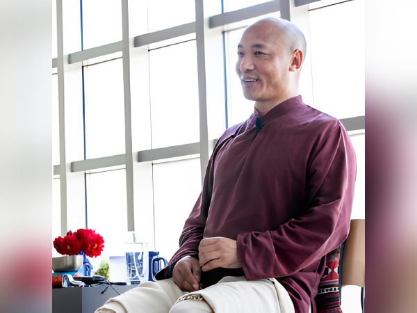 Man in maroon sweater meditating by a window with natural light.