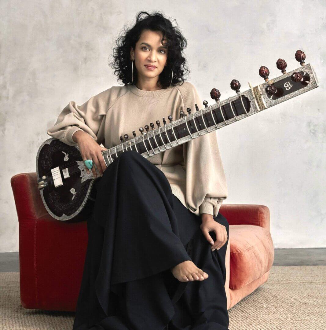 A woman sitting on a red chair holding a sitar.