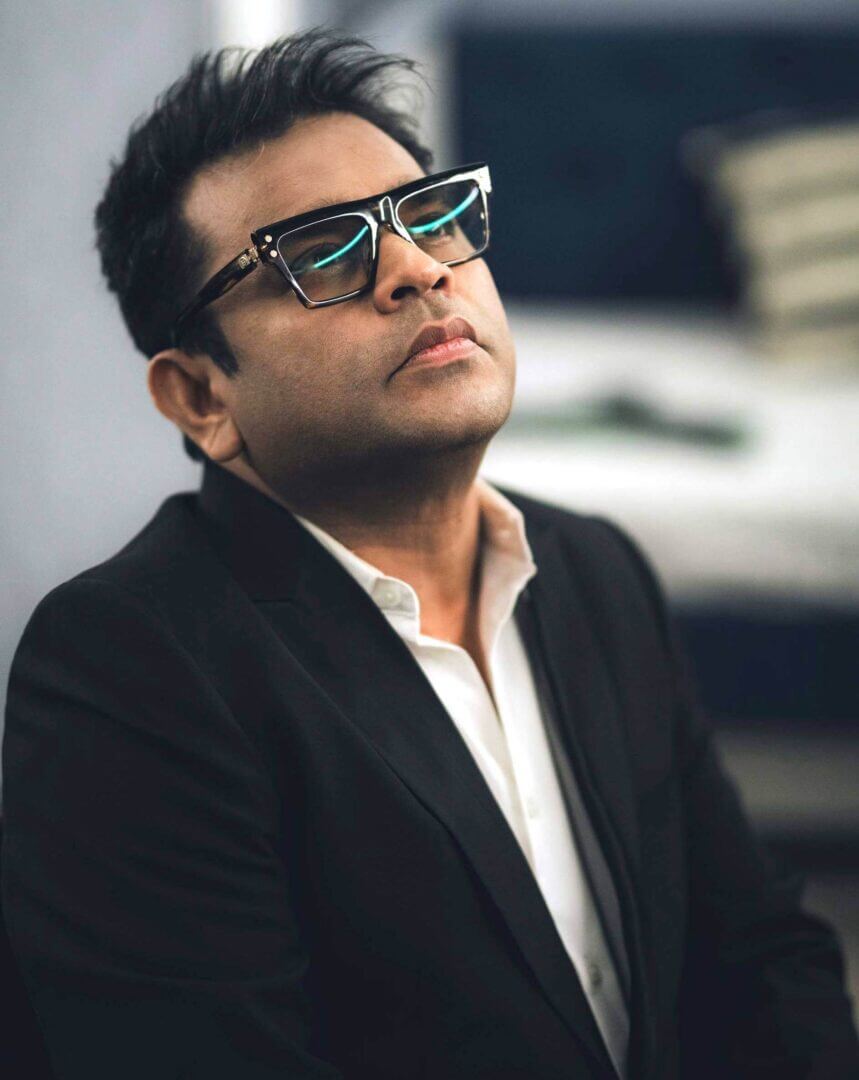 Man in a black suit wearing sunglasses, looking upwards.