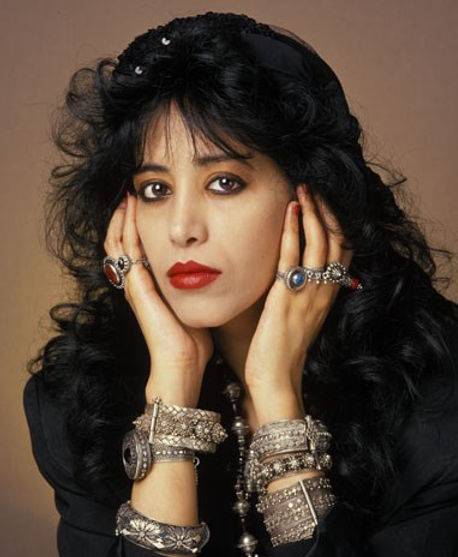 Woman with dark hair, bold makeup, and multiple rings and bracelets.