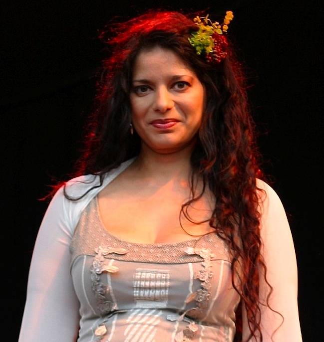 A woman with long curly hair and a floral hair accessory.