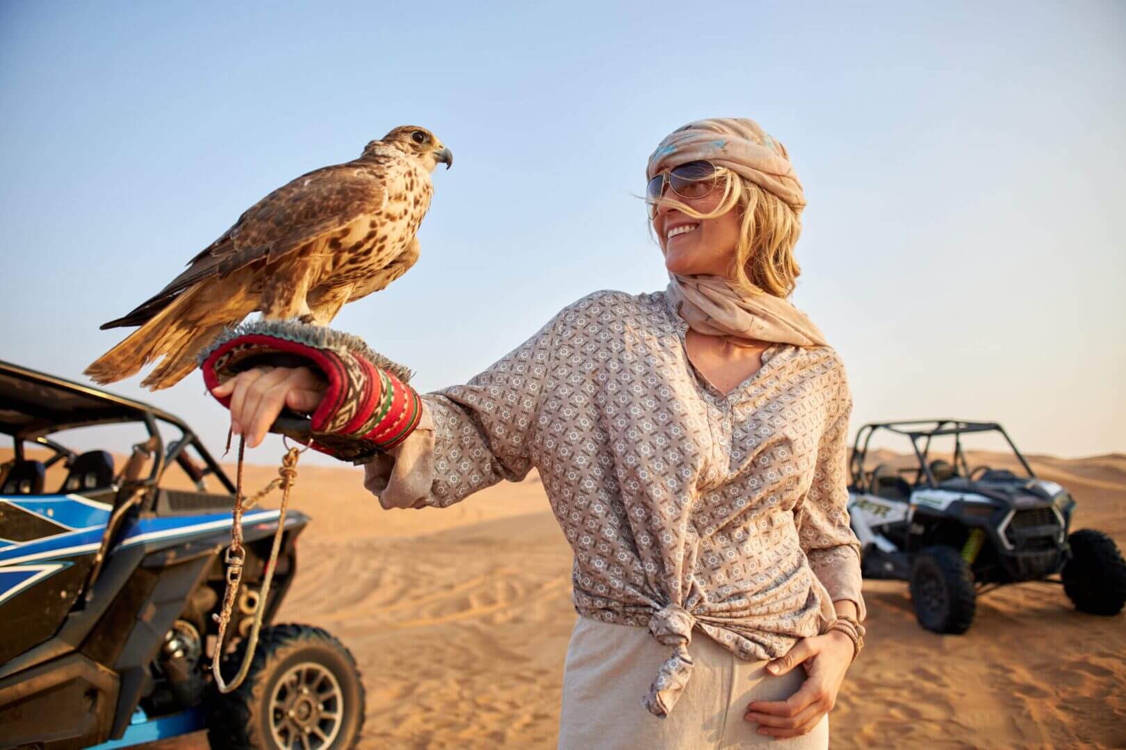 Person holding falcon in desert with buggies.